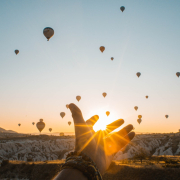 Photo of Person's Hand Across Flying Hot Air Balloons During Golden Hour