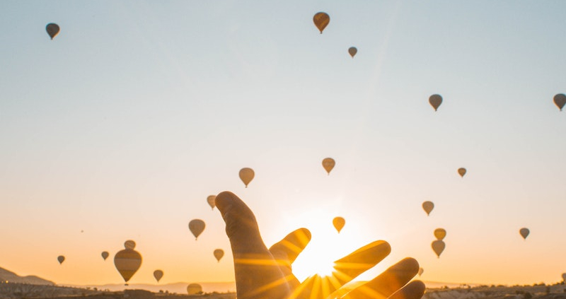 Photo of Person's Hand Across Flying Hot Air Balloons During Golden Hour